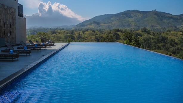 A swimming pool with lounge chairs and a view of green hills. - Sajjan Bagh Resort Kumbhalgarh (Kumbhalgarh)