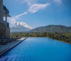 Una piscina con sillones de descanso y vistas a colinas verdes.
