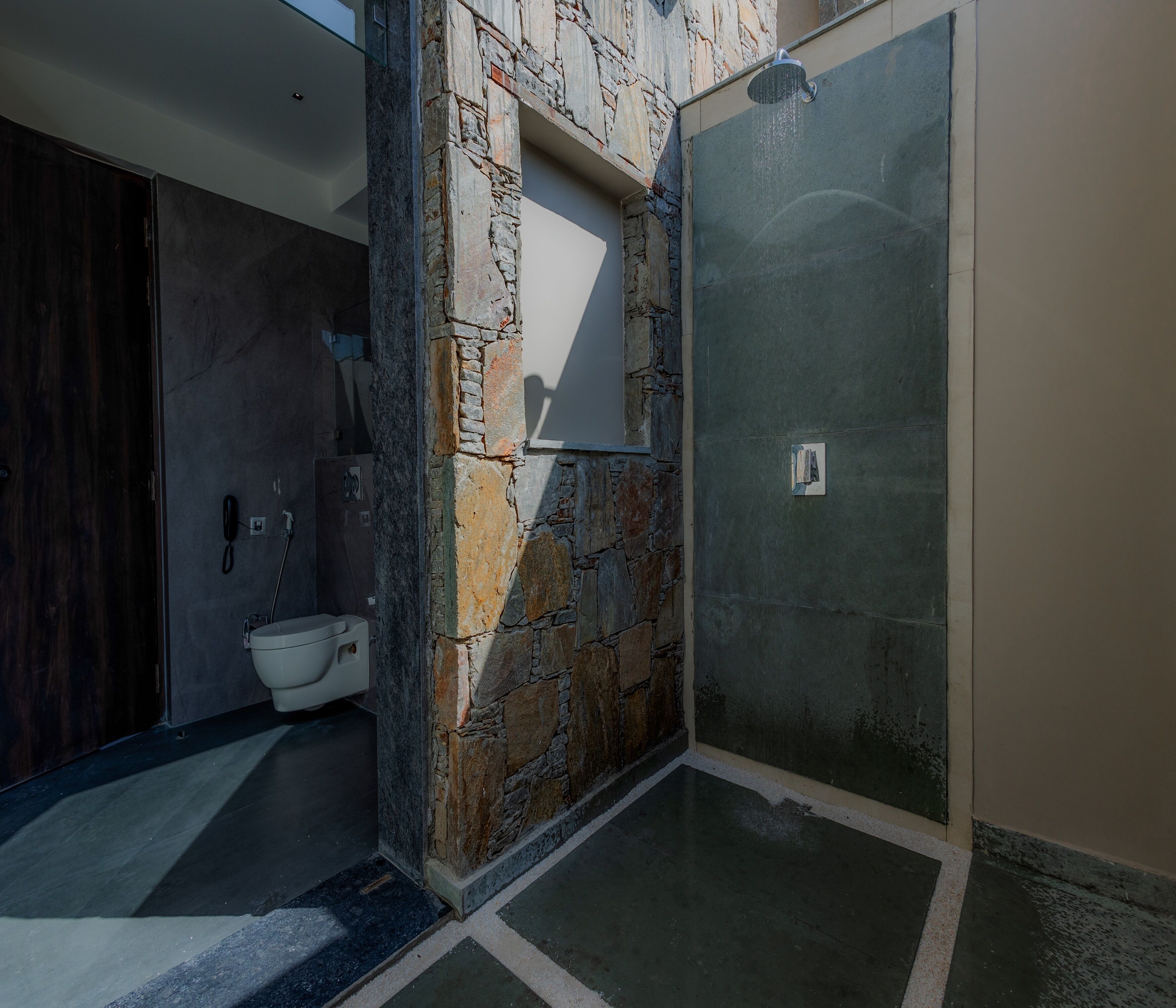 A bathroom with a stone wall, a toilet, and a shower area.