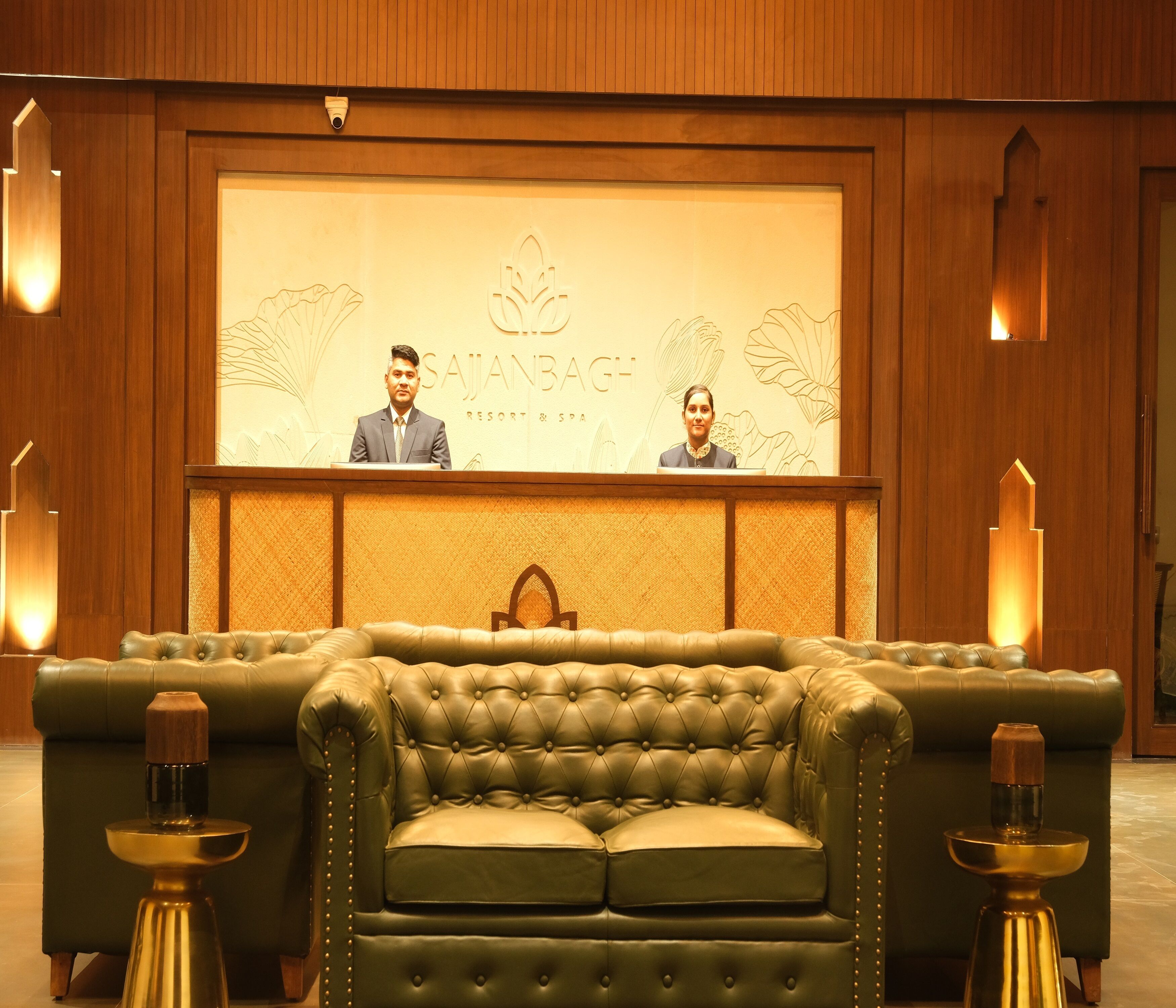 A reception area with a reception desk, two staff members, and a green leather sofa.