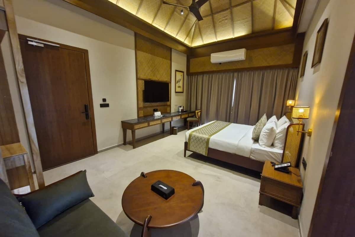A hotel room with a bed, a sofa, a round table, a desk, and a ceiling fan.