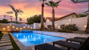 A swimming pool with lounge chairs, palm trees, and string lights.