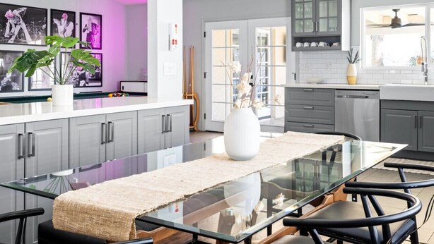 A modern kitchen with grey cabinets, a glass dining table, and a large window.