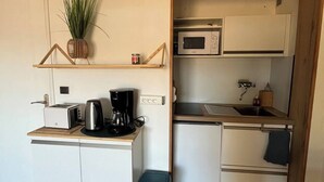A compact kitchen with a microwave, toaster, and coffee maker on a wooden countertop, a small trash bin, and a potted plant on a shelf. - Studio à Gréoux les Bains - Les Fontaines (Gréoux-les-Bains)