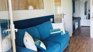 A modern living room with a blue sofa, a large woven wall hanging, and a wooden floor. - Studio à Gréoux les Bains - Les Fontaines (Gréoux-les-Bains)