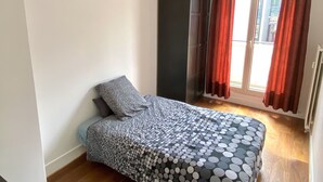 A bedroom with a bed, a window with curtains, a hanging light fixture, and a radiator. - Apartment near Parc des Buttes Chaumont - 4 bedrooms (Paris)