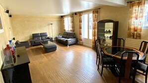 A spacious living room with a wooden floor, a sofa set, a dining table with chairs, and a large mirror. - Apartment near Parc des Buttes Chaumont - 4 bedrooms (Paris)