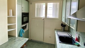 A compact kitchen with a built-in oven, a window with blinds, a sink, and a countertop with a dish rack. - Apartment near Parc des Buttes Chaumont - 4 bedrooms (Paris)