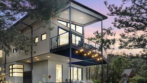 Una casa moderna de dos pisos con balcón, ventanas amplias y jardín.