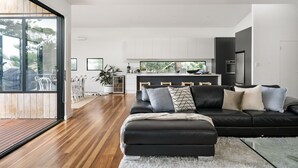 Una sala de estar moderna con un sofá de cuero negro, piso de madera y una mesa de comedor de vidrio.