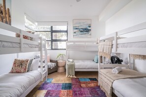 Una habitación con literas, un tapete colorido, una ventana con vistas y un cuadro en la pared.