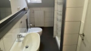 Kapea kylpyhuone, jossa on kattovalokuvio, pesuallas ja wc-istuin.