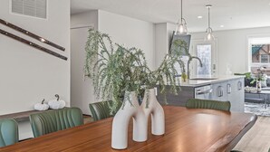 Un comedor con una mesa de madera, sillas verdes y tres jarrones blancos con plantas.