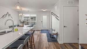 Cocina moderna con una isla central, taburetes de bar, una lámpara colgante y vistas al jardín trasero a través de una puerta de vidrio.