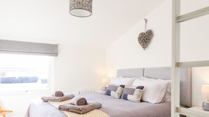Une chambre à coucher bien rangée, avec un grand lit, une table de chevet, un luminaire suspendu et une fenêtre équipée de stores.