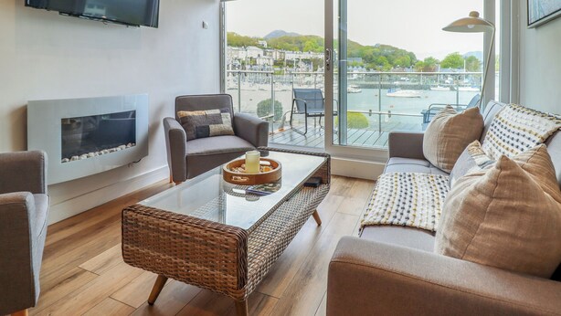 Un salon moderne doté d’un téléviseur, de sièges confortables, d’une table basse en verre et offrant une vue sur un port de plaisance.