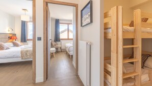 A hotel room with a wooden floor, a bed with a white duvet, a chair, a desk, and a radiator. - Lovely 6-person apartment, close to slopes, WiFi, pets allowed (Huez)