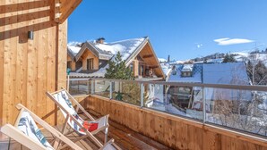 A wooden deck with two lounge chairs, a glass balustrade, and a view of snow-covered houses. - Lovely 6-person apartment, close to slopes, WiFi, pets allowed (Huez)