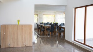 A spacious dining area with a wooden cabinet, a large window, and a view of a room with a bed.