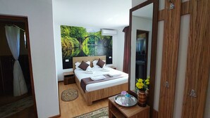 Un dormitorio con cama, espejo, mesita de noche con un florero, y vista a un jardín a través de la ventana.