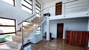 Un interior amplio con una escalera que sube a un nivel superior, un mostrador de recepción y un suelo con diseño.