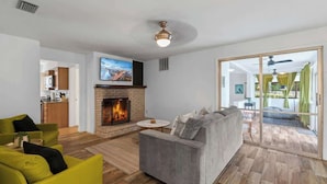 Een woonkamer met een open haard, een bank, een salontafel en uitzicht door een glazen deur op een terras.