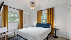 Een slaapkamer met een bed, een stoel, een nachtkastje met lamp en een raam met gordijnen.