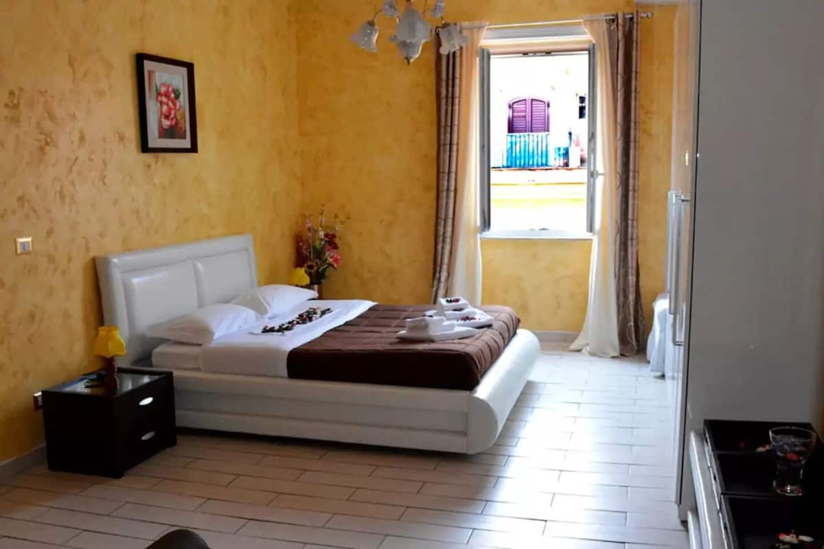 Un dormitorio con cama, mesita de noche, ventana con cortinas y vistas al exterior.