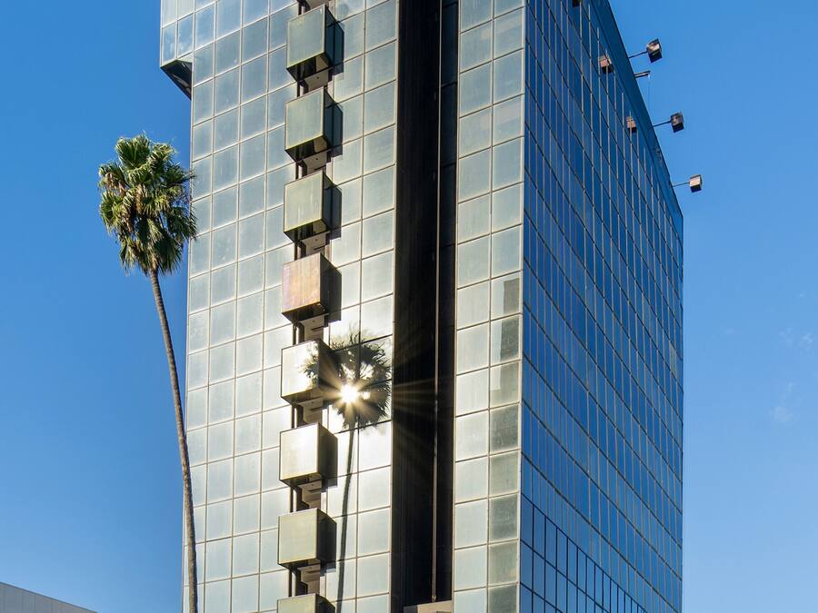 Um edifício moderno de vidro com fachada refletora, uma palmeira na frente e um céu azul claro.
