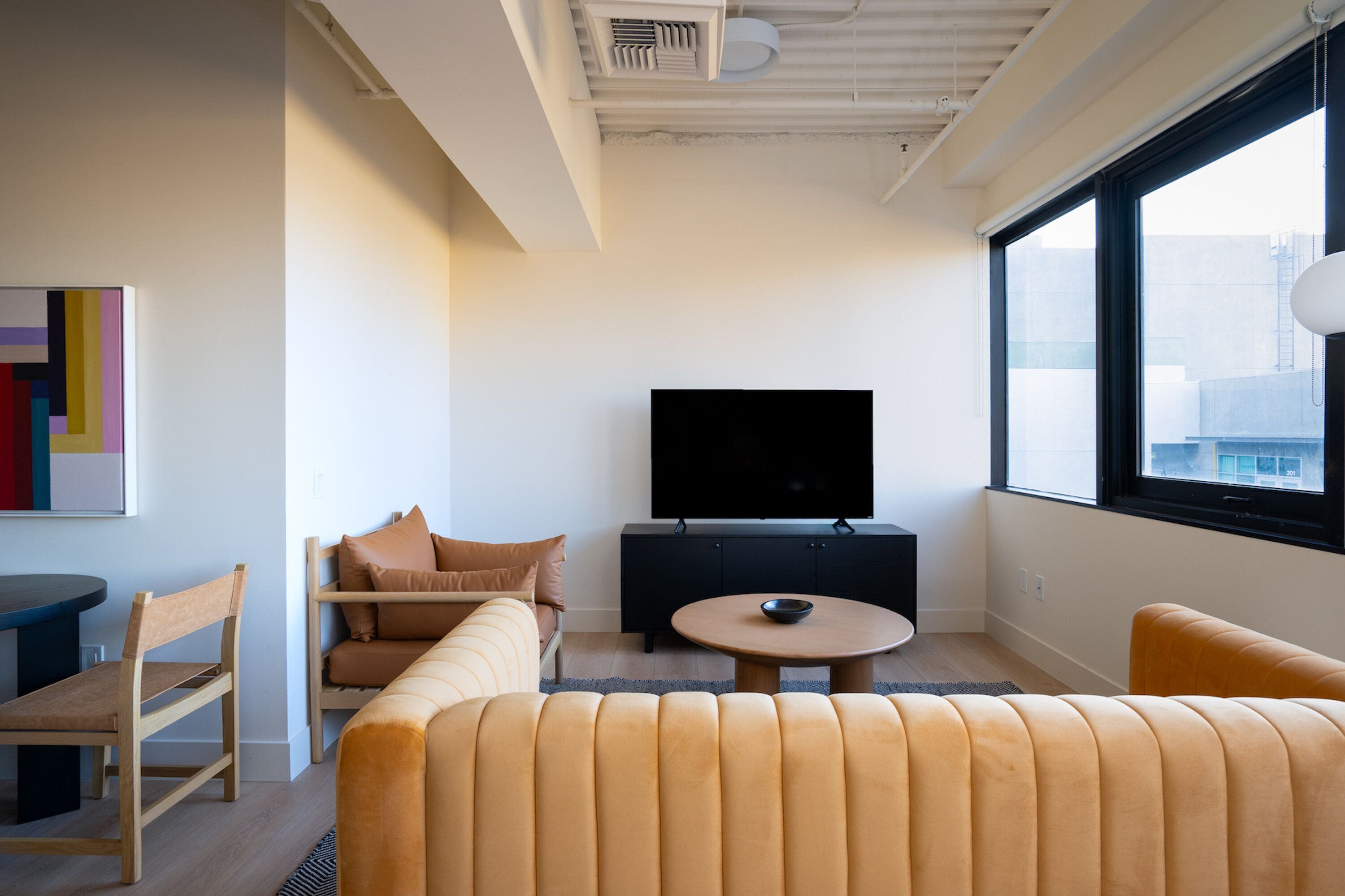 Uma sala de estar moderna com sofá, mesa de centro, televisão e janela com vista para a cidade.