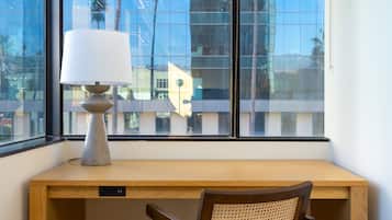 Un bureau d’angle avec une lampe, une chaise et une vue sur un immeuble moderne par la fenêtre.