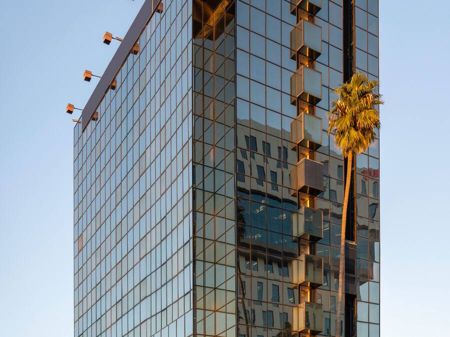 Um edifício moderno de vários andares com fachada de vidro e um elemento estrutural vertical central.