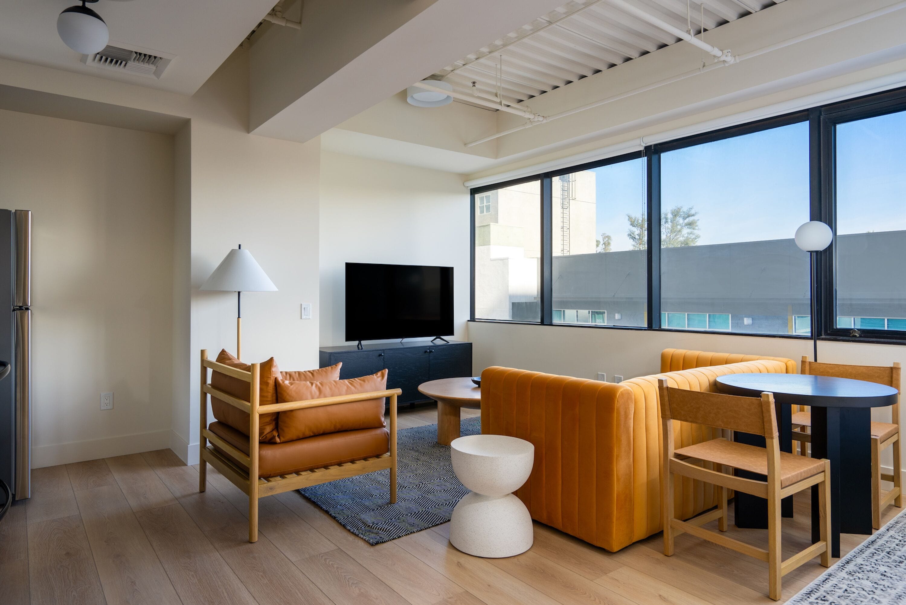 A modern living room with a sofa, a coffee table, a TV, and a dining table with chairs.