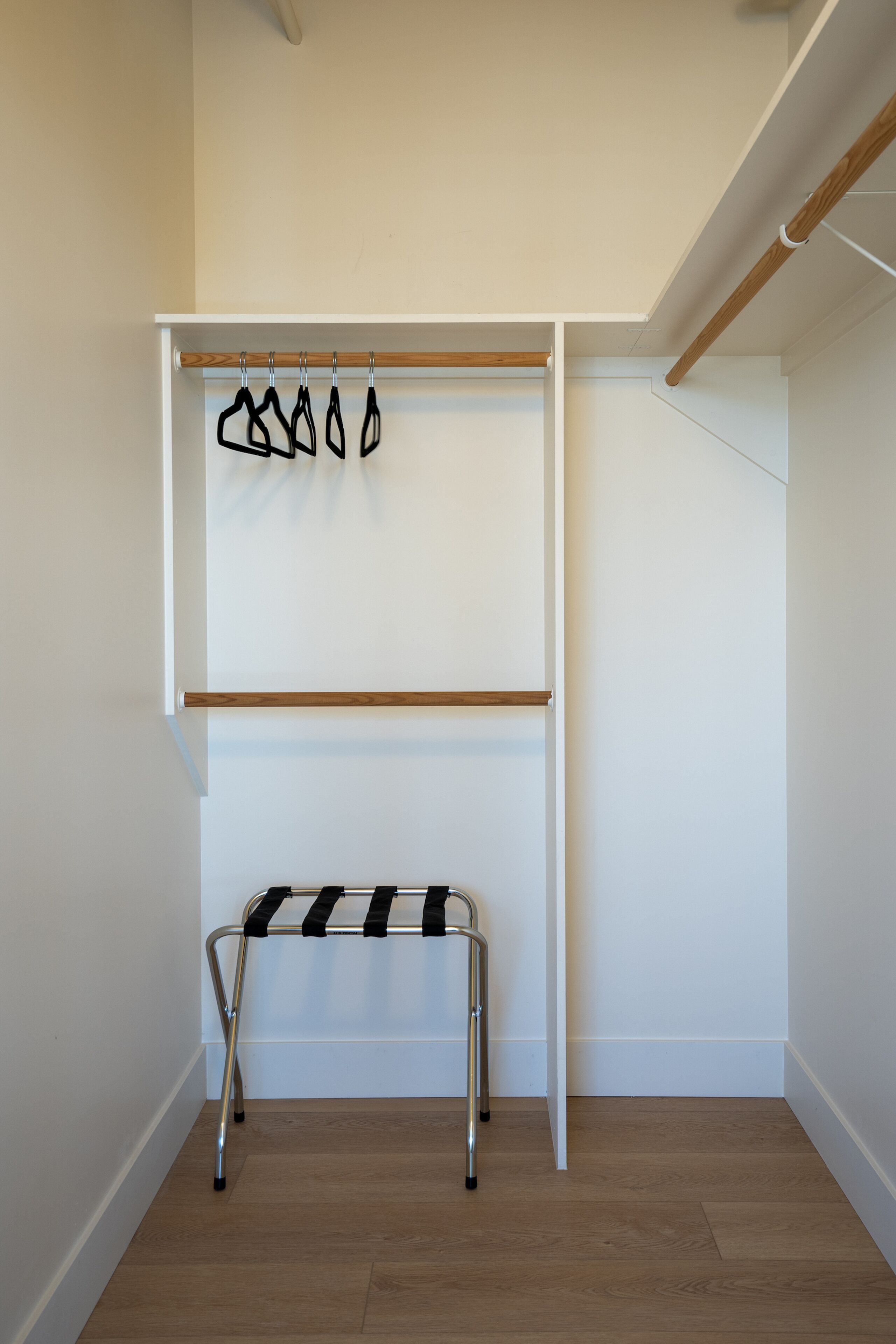 A room with a wooden floor, a white wall, and a metal bench with a black and white striped seat.