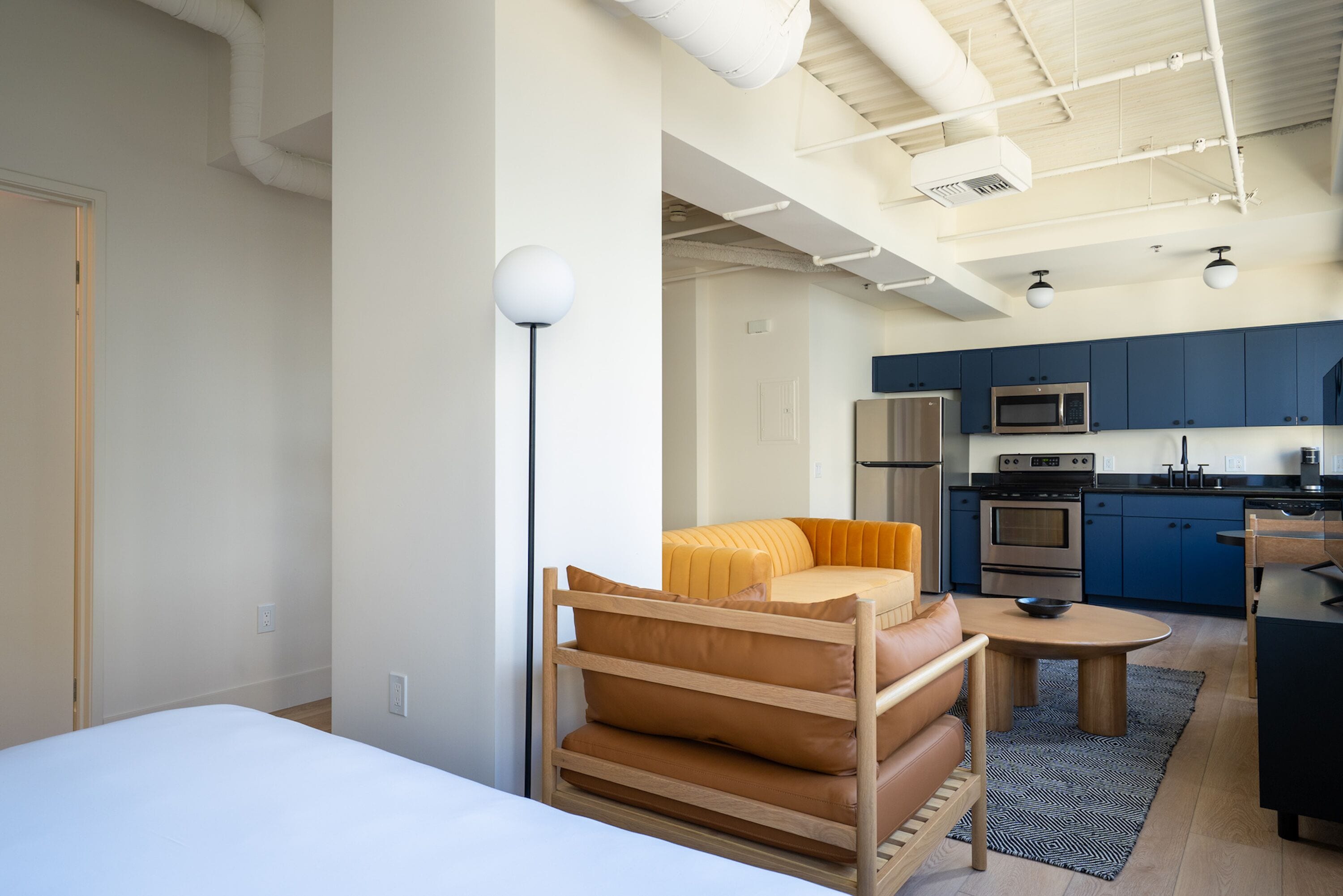 A modern apartment with a bed, a sofa, a dining table, and a kitchen area.