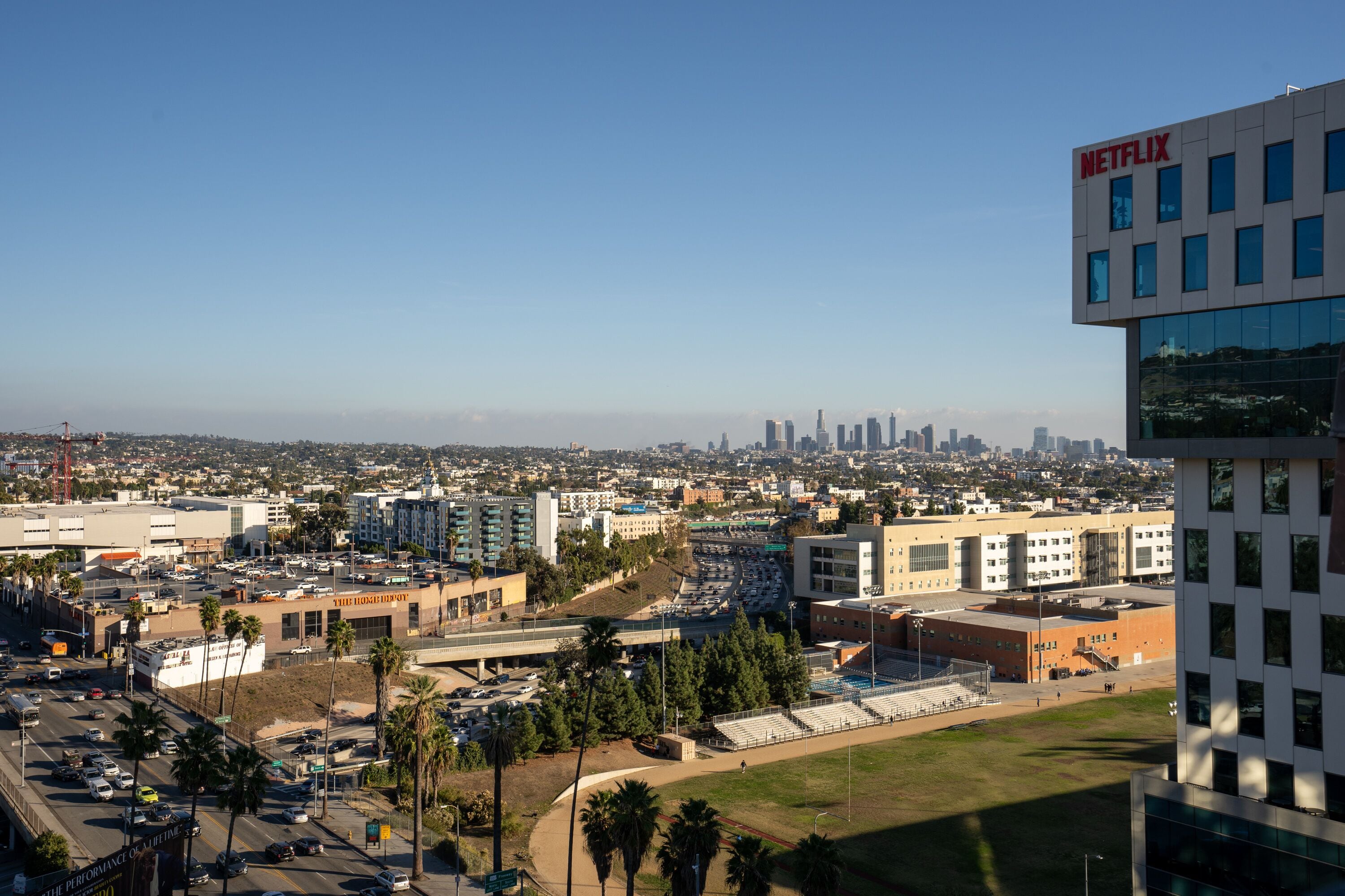 Ein modernes Gebäude mit gut sichtbarem Netflix-Logo, umgeben von einem Parkplatz und einer Skyline im Hintergrund.