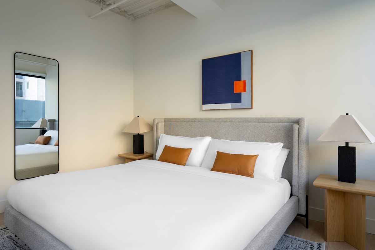 A modern hotel room with a large bed, two bedside tables, a mirror, and a painting on the wall.