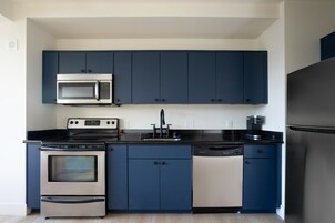 Een moderne keuken met donkerblauwe kastjes en roestvrijstalen apparatuur, waaronder een magnetron, fornuis, vaatwasser en koelkast.