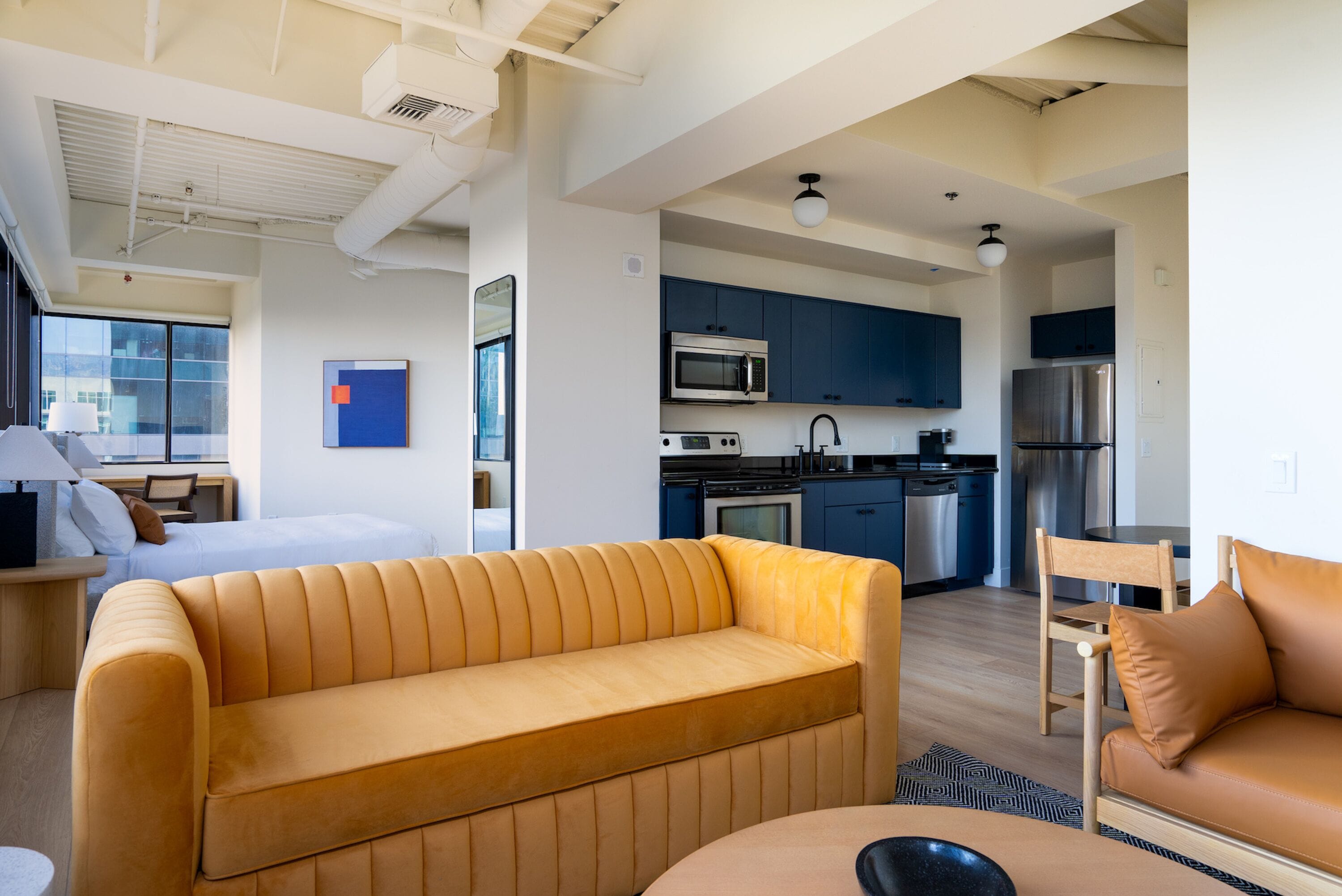 A modern hotel room with a sofa, a dining table, and a kitchenette.