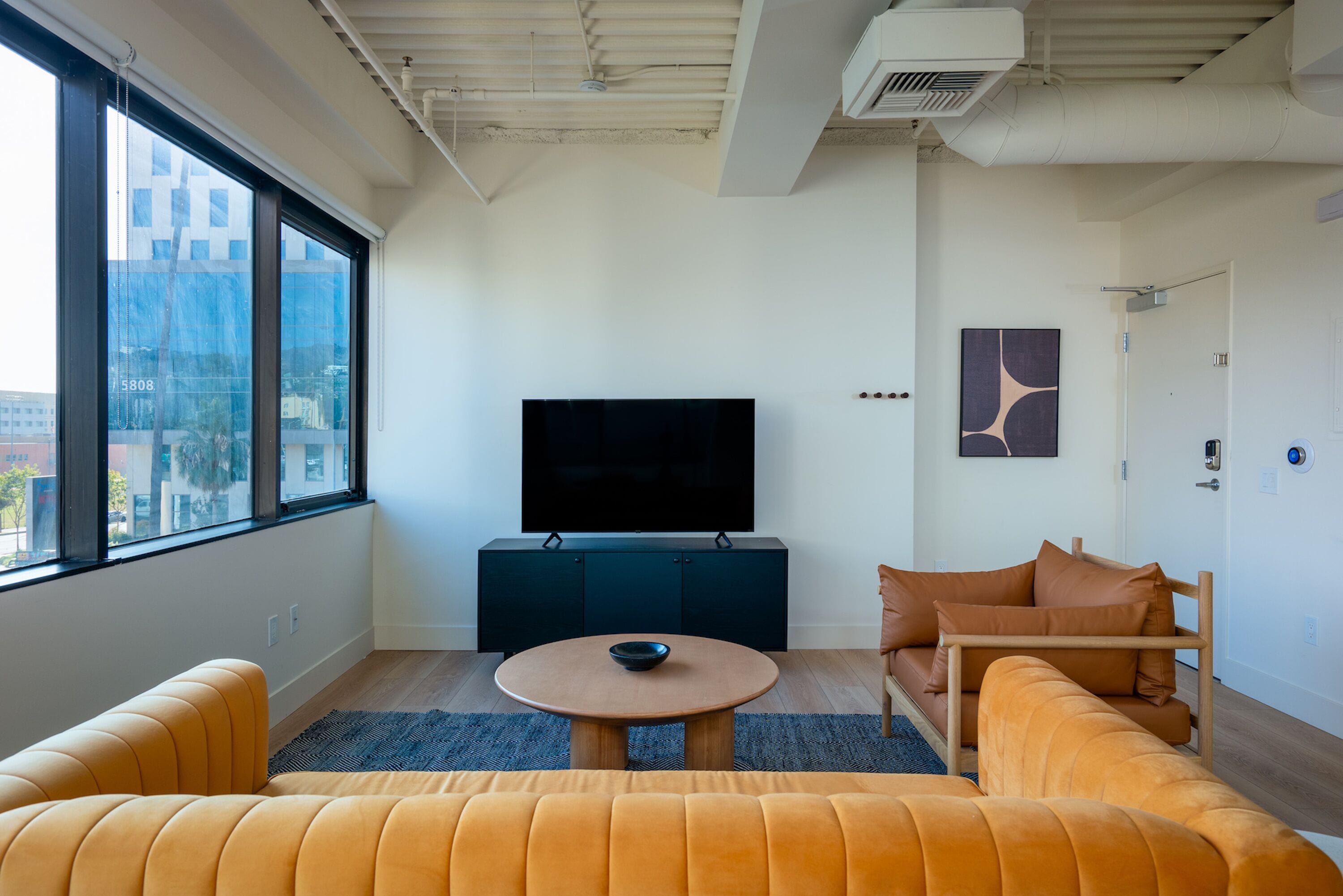 A modern living room with a large window, a flat-screen TV, a round coffee table, and a sofa.