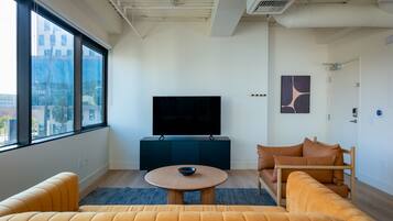 A modern living room with a large window, a flat-screen TV, a round coffee table, and a sofa.