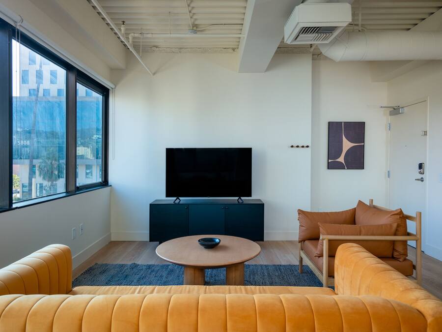 A modern living room with a large window, a flat-screen TV, a round coffee table, and a sofa.