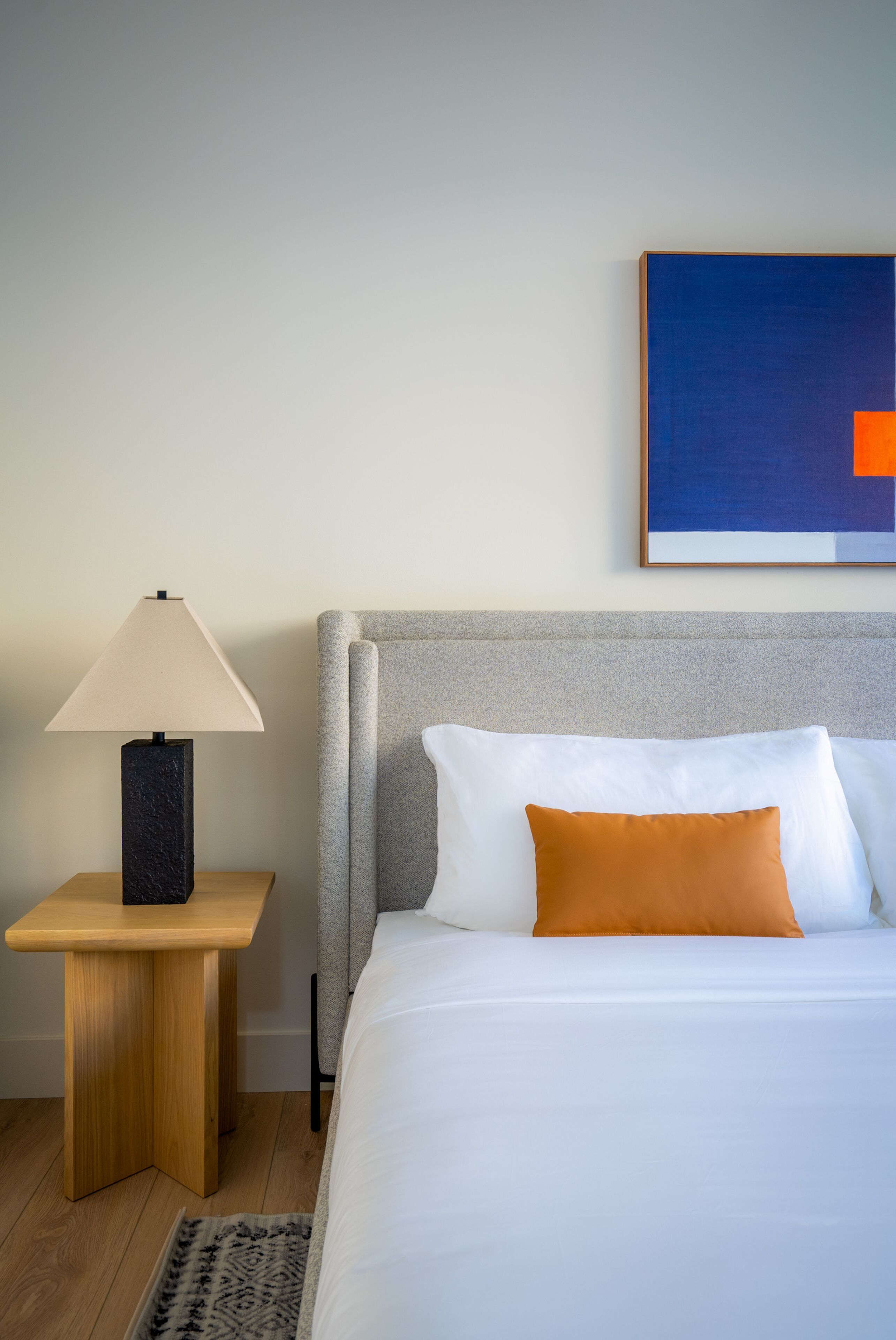 A neatly arranged hotel room with a bed, a nightstand with a lamp, and a framed artwork on the wall.