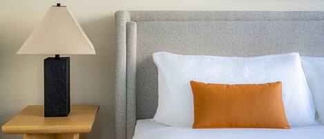 A neatly arranged hotel room with a bed, a nightstand with a lamp, and a framed artwork on the wall.