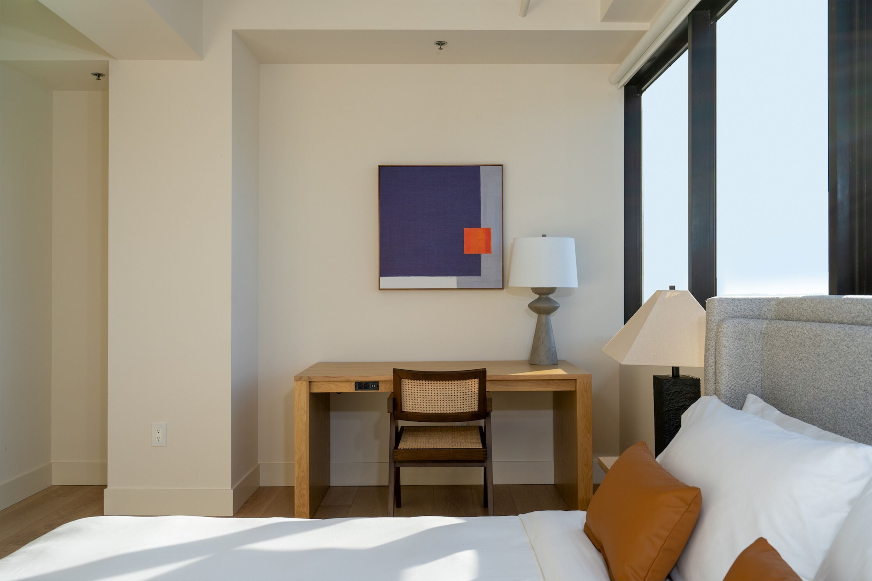 Une chambre d’hôtel avec un lit, un bureau, une chaise, une lampe et une fenêtre.