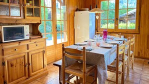 A wooden cabin interior with a dining table set for four, wooden cabinets, a microwave, and a refrigerator. - Family chalet near slopes with WiFi and parking (Les Gets)