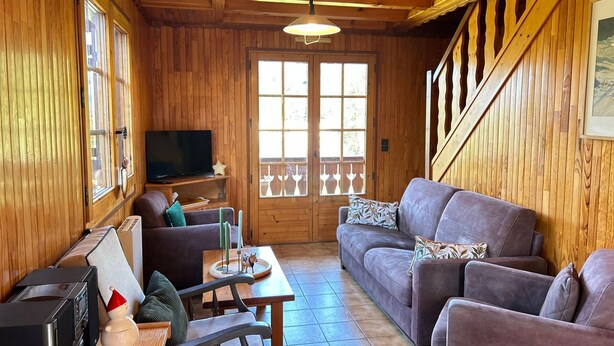 A cozy wooden interior with a sofa, a television, and a dining table. - Family chalet near slopes with WiFi and parking (Les Gets)