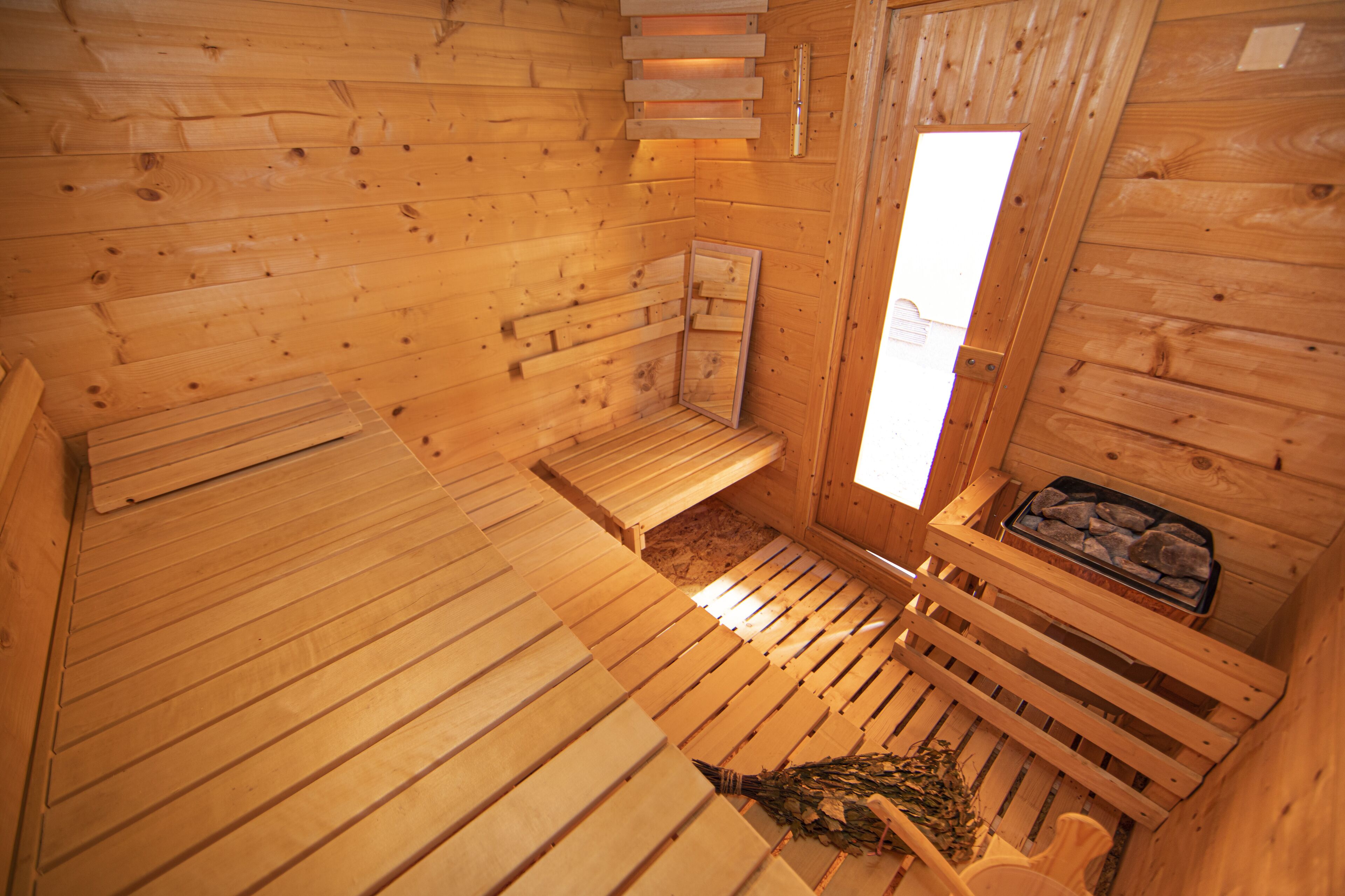 A wooden sauna with benches, a window, and a tray of stones.