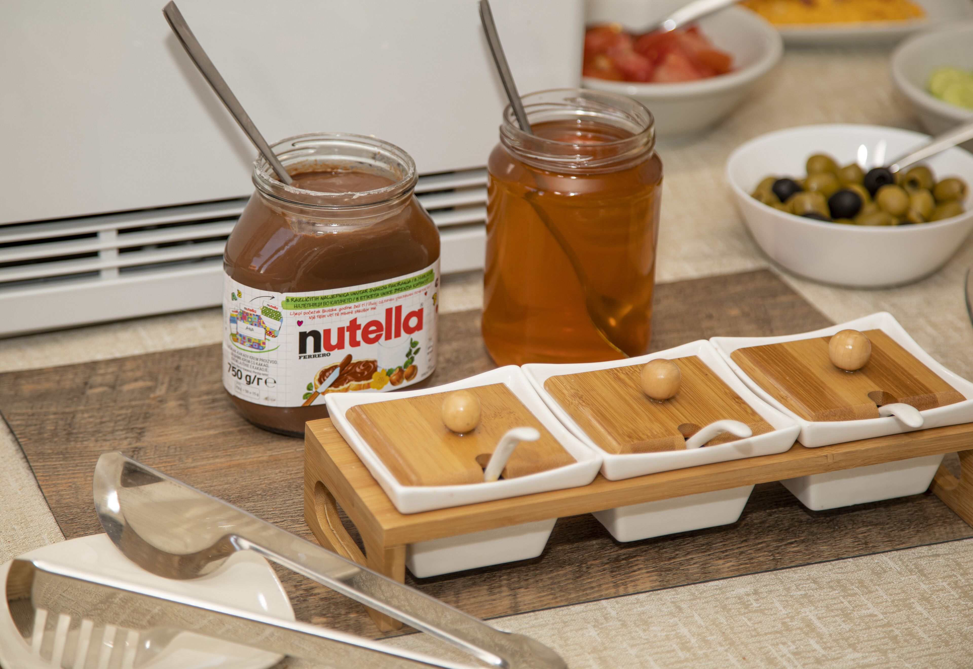 Un plan de travail de cuisine avec un pot de Nutella, un pot de miel et une planche à découper en bois, sur laquelle repose une cuillère.