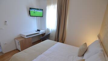 Una habitación de hotel con cama, escritorio y televisor de pantalla plana, además de una ventana con cortinas.